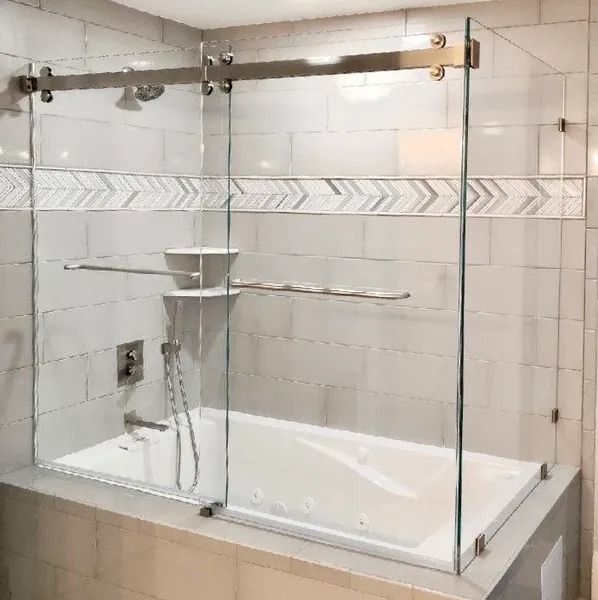 A white jetted bathtub with a frameless sliding glass door enclosure in a tiled bathroom with chevron accent tiling.