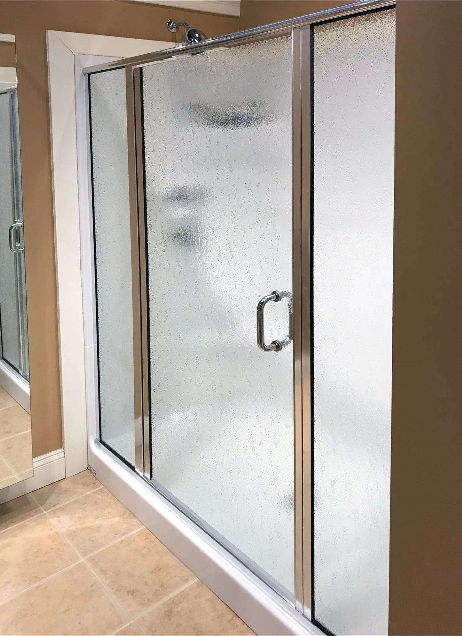 A walk-in shower with a silver-framed, textured glass door and a rectangular handle in a tiled bathroom.