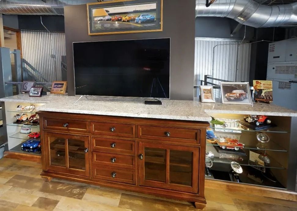 A wooden media console with a television sits between two glass-shelved display cabinets containing toy cars.