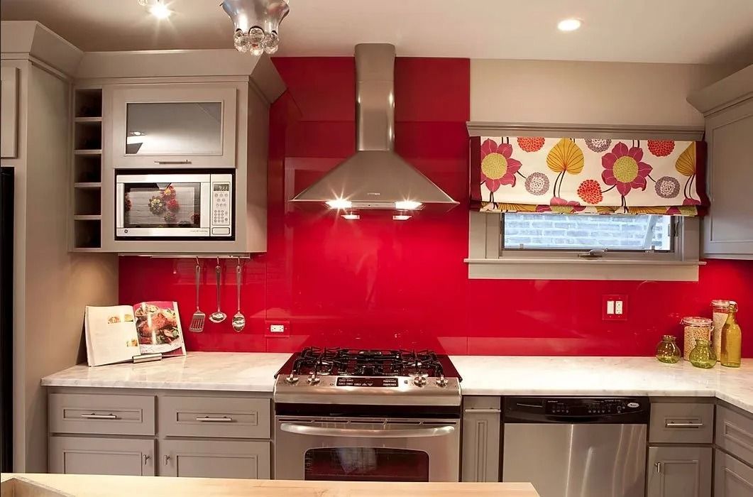 A modern kitchen featuring grey cabinets, a vibrant red glass backsplash, stainless steel appliances, and a floral valance.