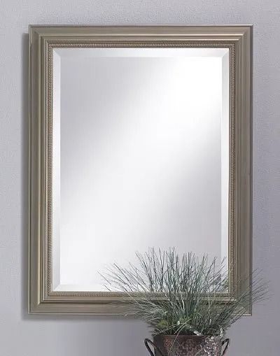 A rectangular wall mirror with a wide, metallic, tiered frame above a potted plant on a plain gray wall.