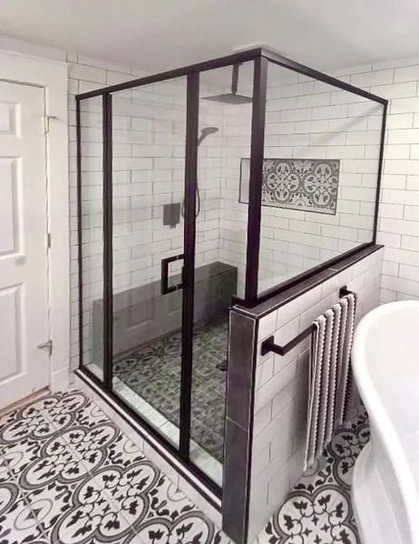 A walk-in shower with a black frame and glass walls, white subway tile, and decorative patterned floor and accent tiles.