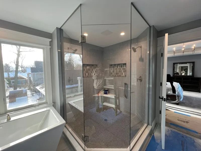 A modern bathroom featuring a white soaking tub, a large glass-enclosed corner shower with tile accents, and open doorway.