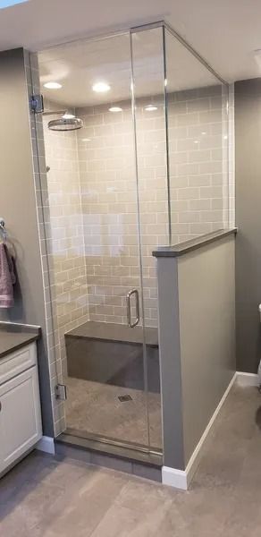 A walk-in shower with a glass door, a built-in stone bench, and light-colored tiled walls in a modern bathroom.