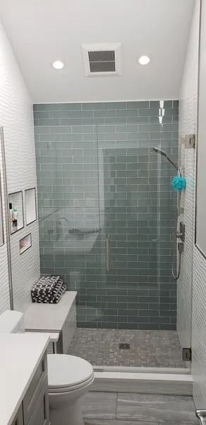 Modern bathroom with a glass-enclosed shower, gray subway tiles, a built-in bench, and a white toilet in the foreground.