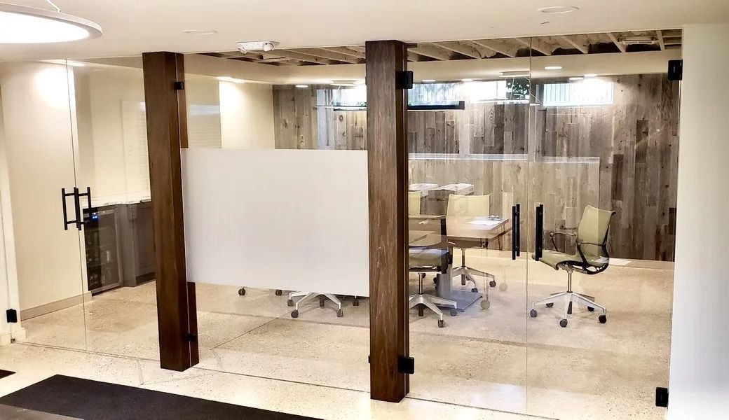 A glass-walled office conference room with wooden support beams and office chairs on a light-colored floor.