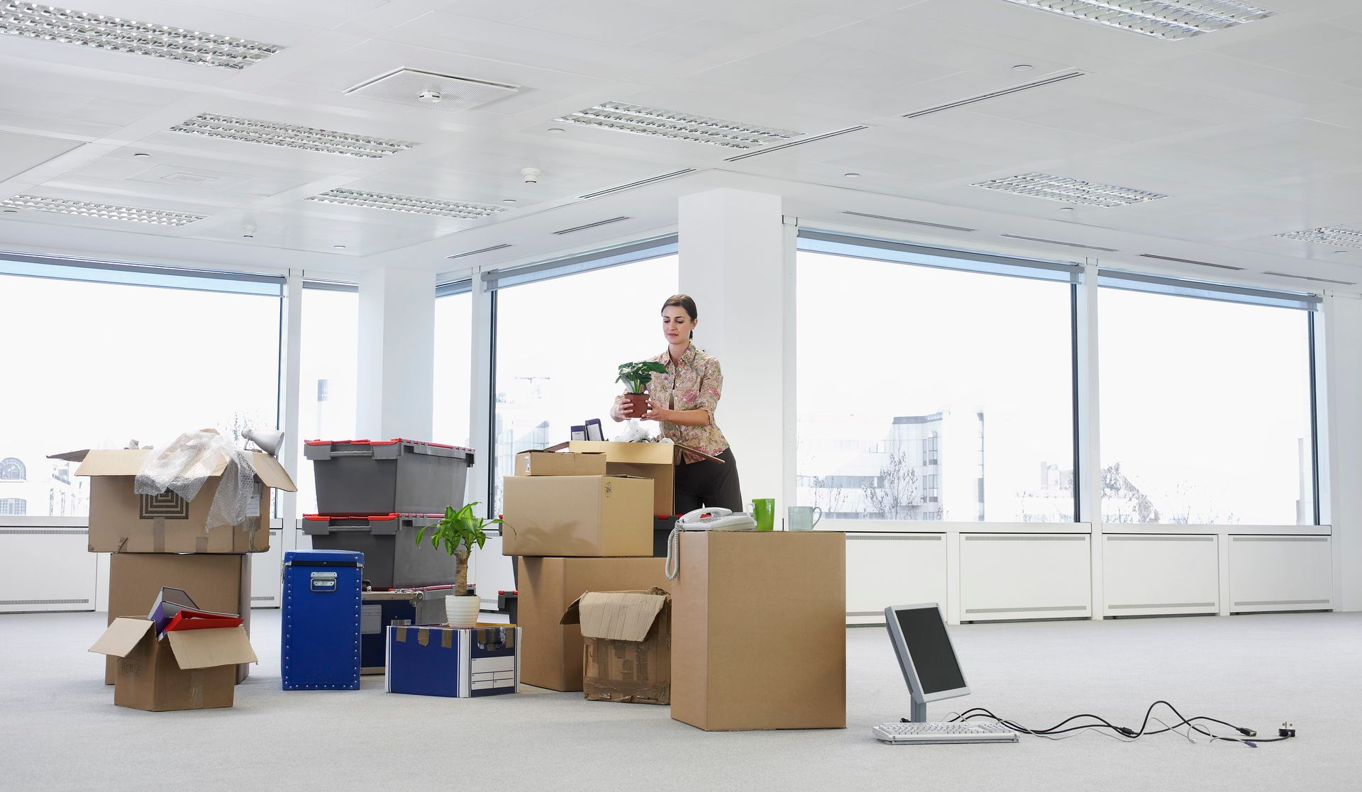 Woman unpacking boxes in an empty office with large windows.