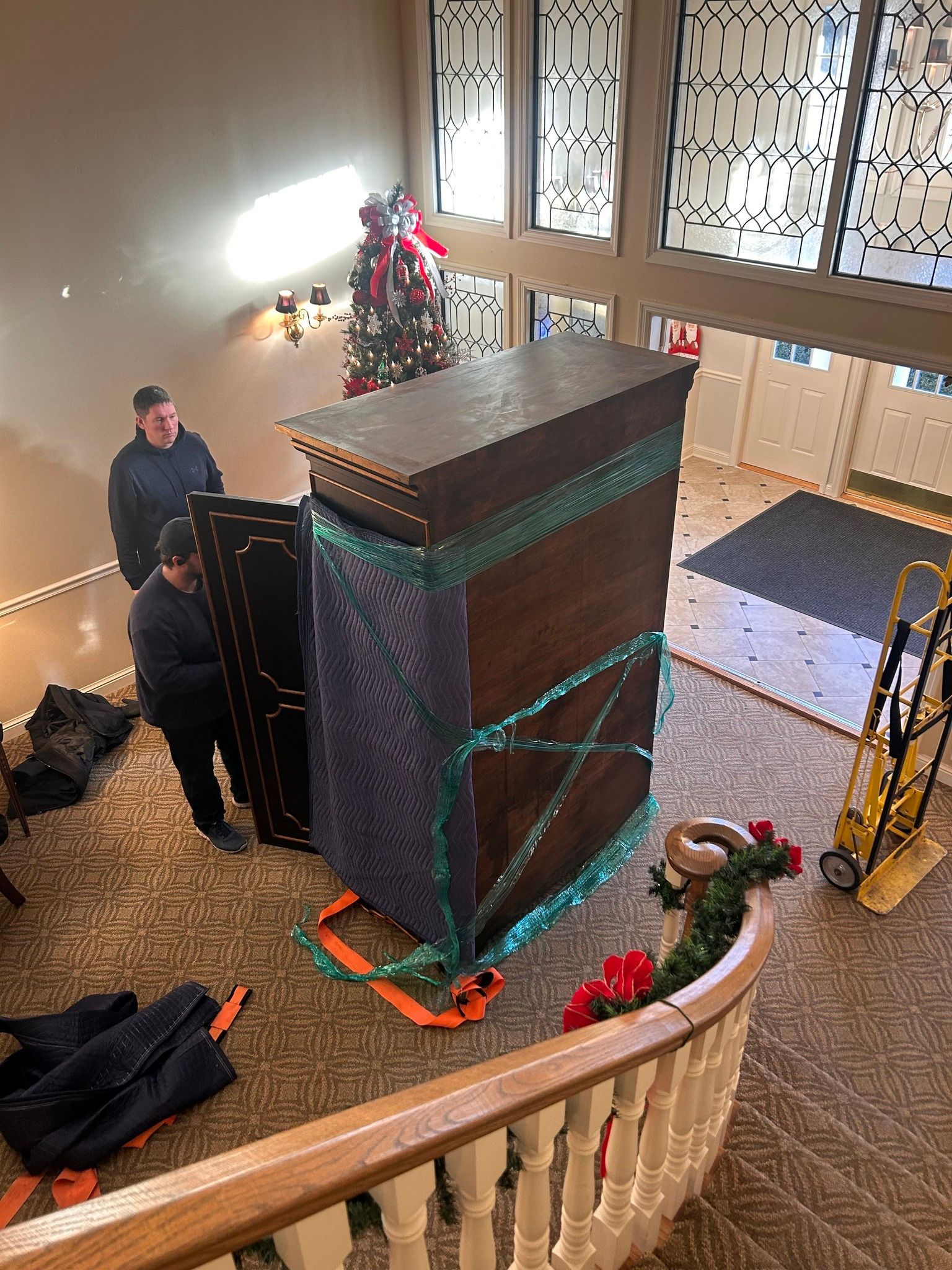 Movers transporting a large wrapped cabinet in a building with a staircase.