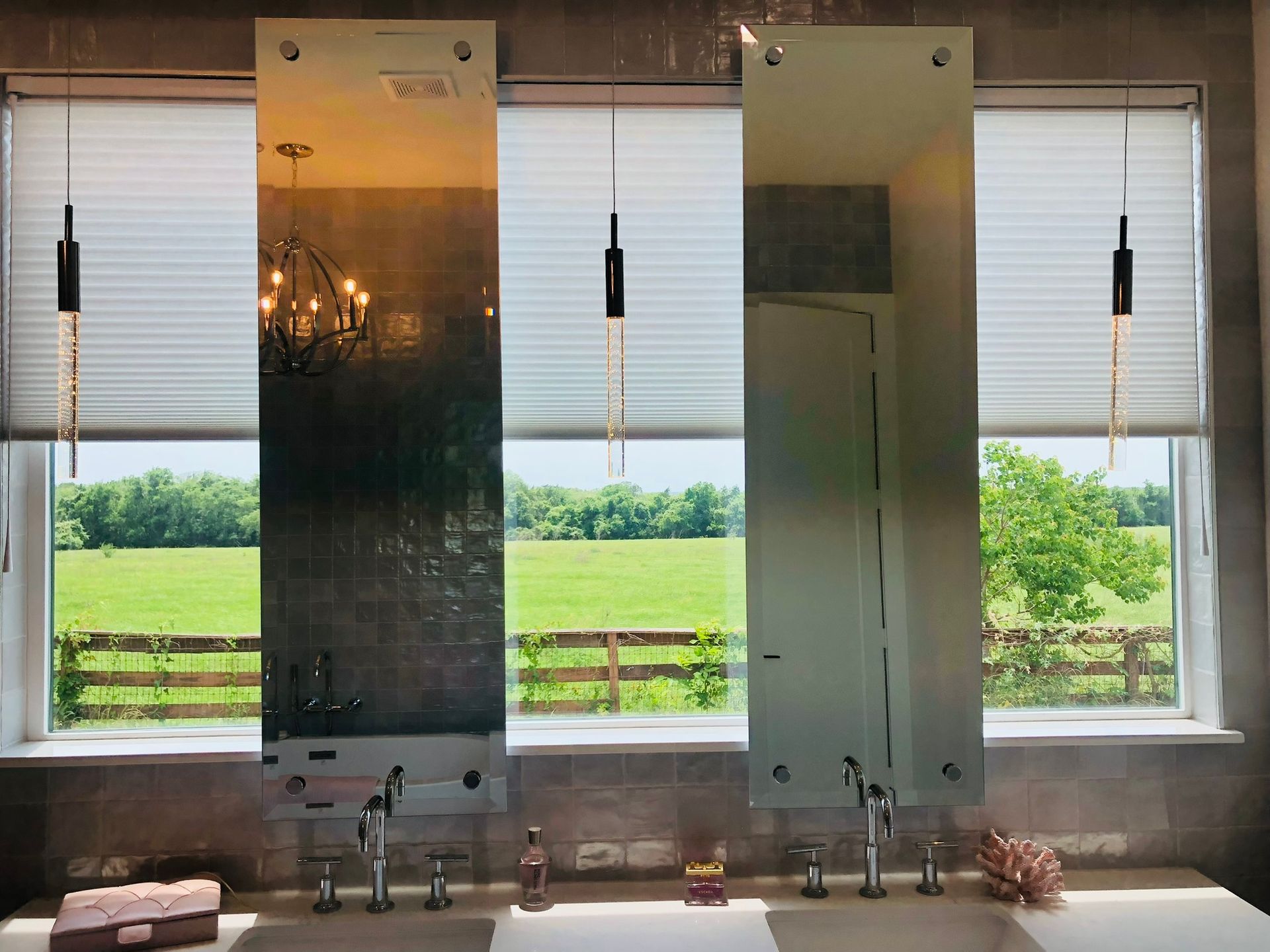 A bathroom with three mirrors and a view of a field.