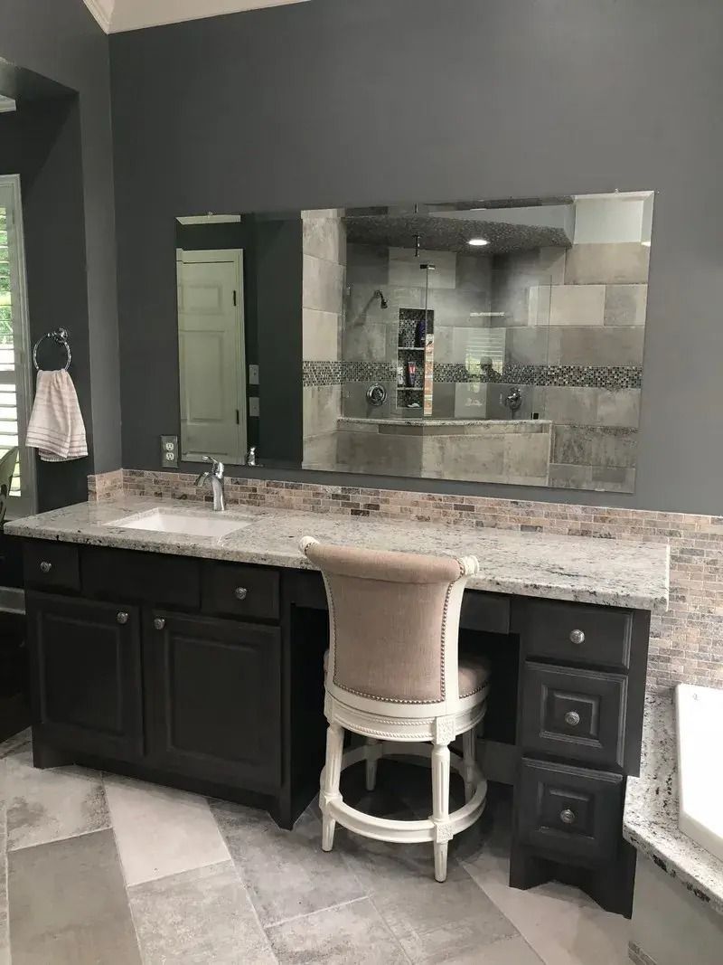 A bathroom with a desk , chair , sink and mirror.