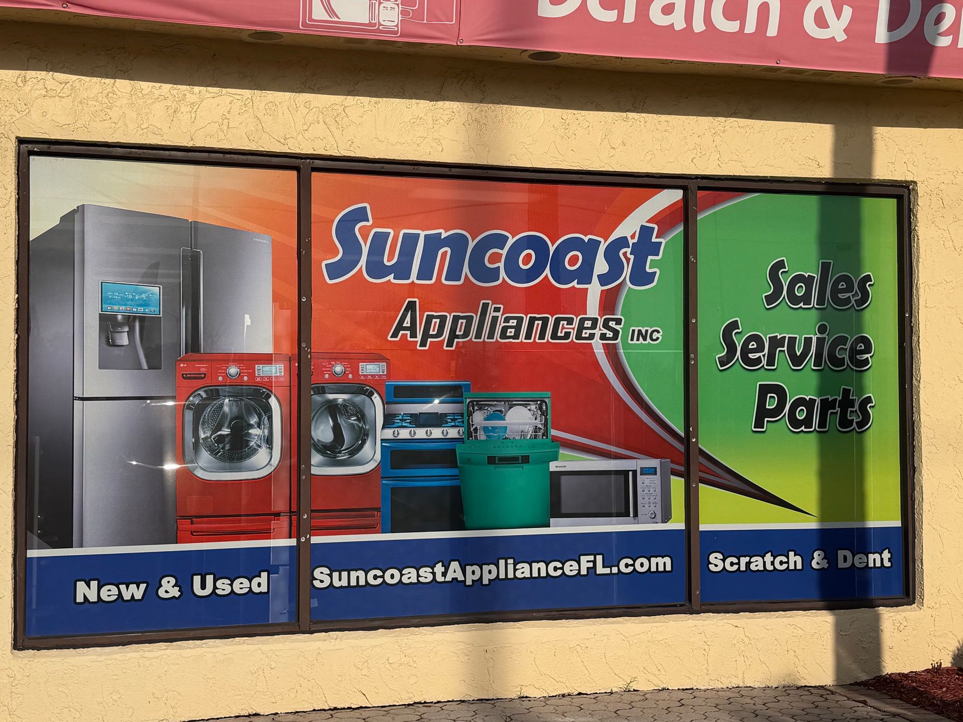 Suncoast Appliance storefront window with sale, service, and parts signs in blue, red, and green.