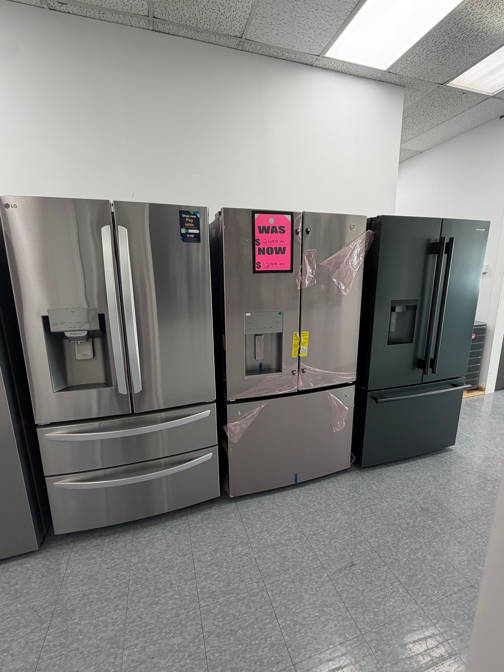 Three stainless steel refrigerators in a commercial kitchen with pink note on the center door.