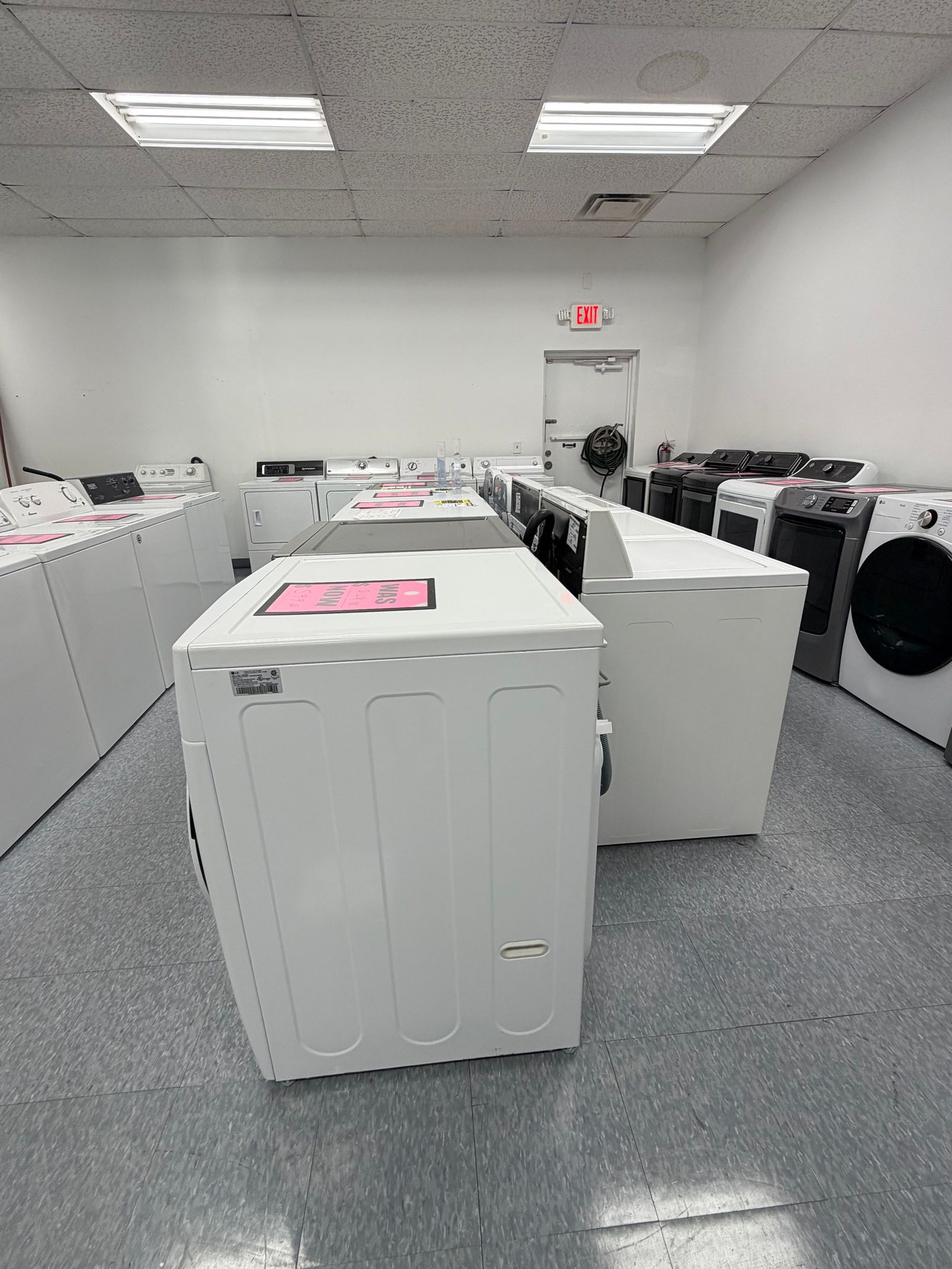 Laundry room with white washers and dryers under fluorescent ceiling lights, one machine open in the foreground