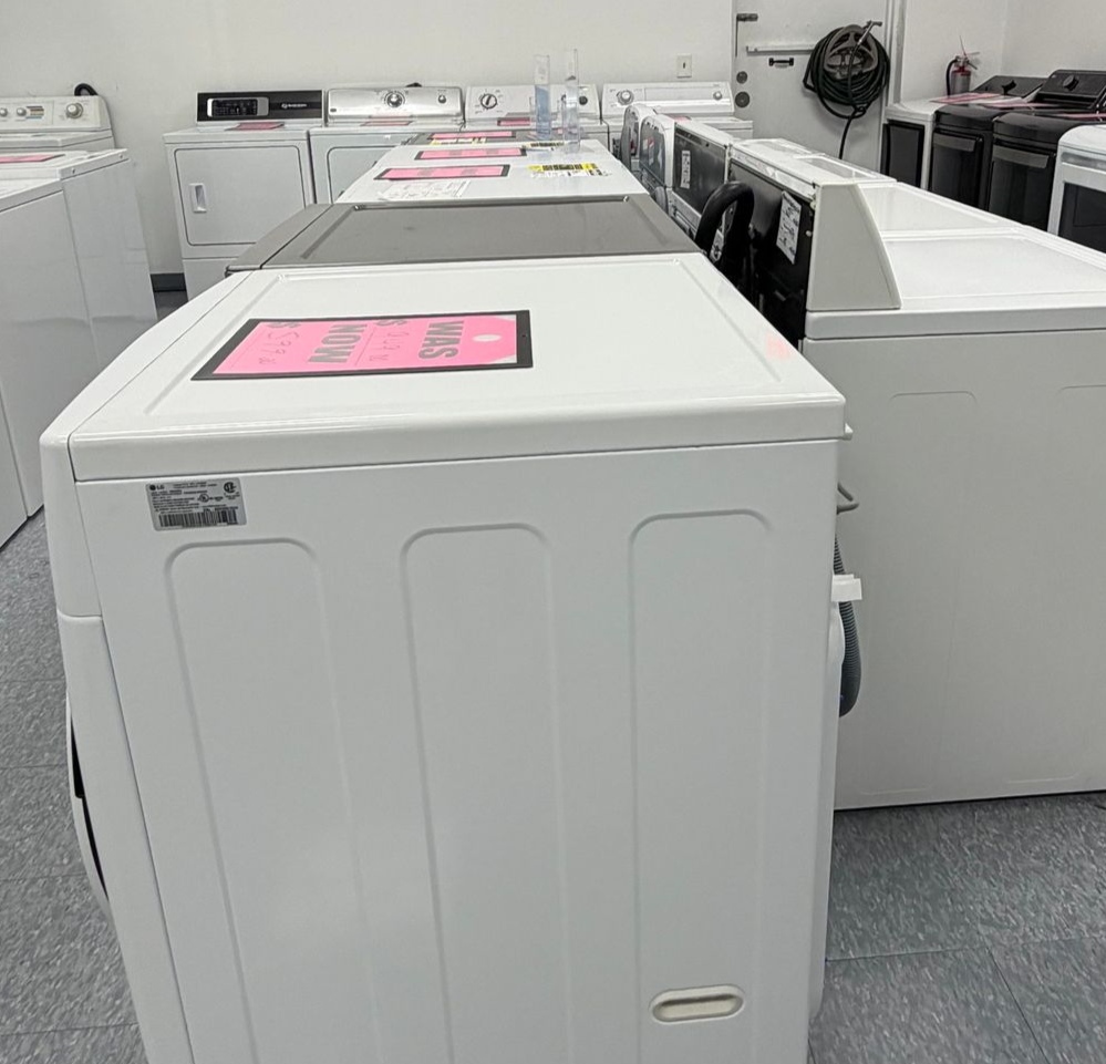 Rows of white washing machines in a laundromat, each with pink signs on top.