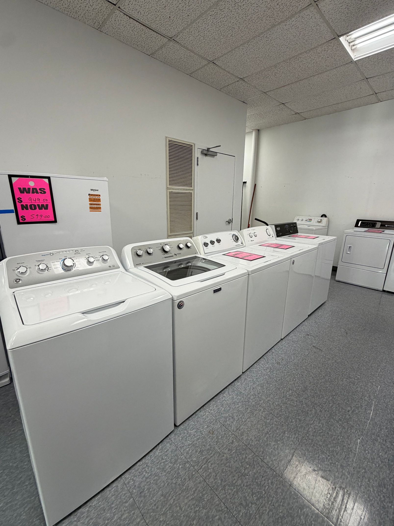 Laundry room with row of white washing machines and dryers under fluorescent lights
