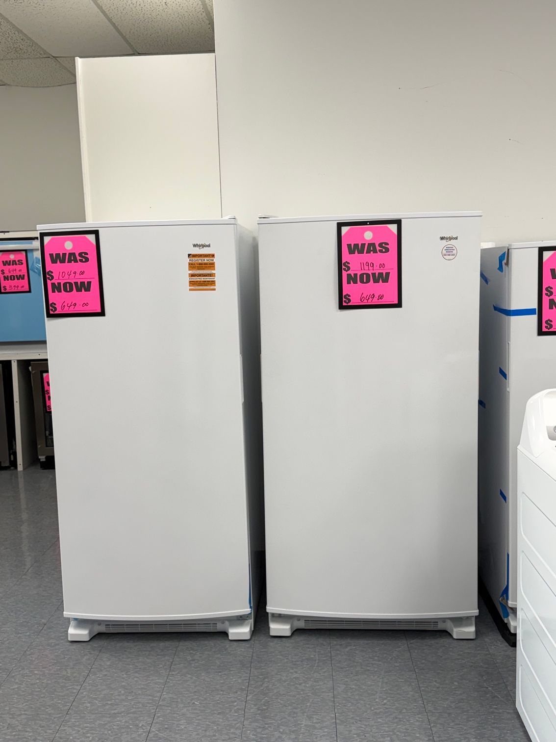 White refrigerators lined up in a store, each with a bright pink sale sign.