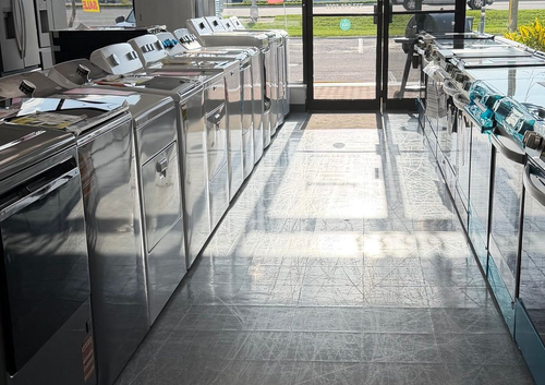 Laundry room with rows of stainless steel washing machines and a glass door at the end