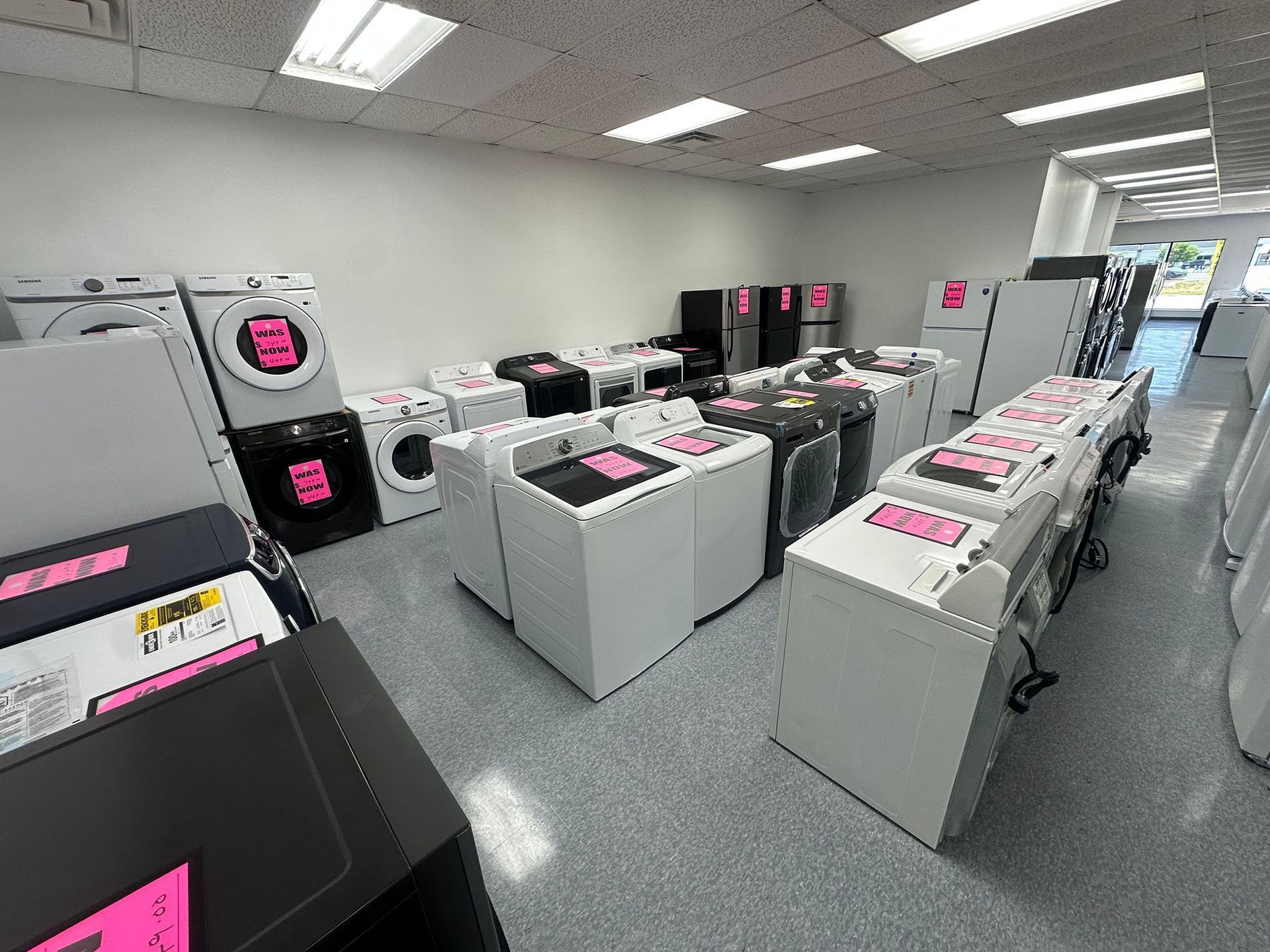 Laundry room with rows of washing machines and dryers, many marked with bright pink sale signs.
