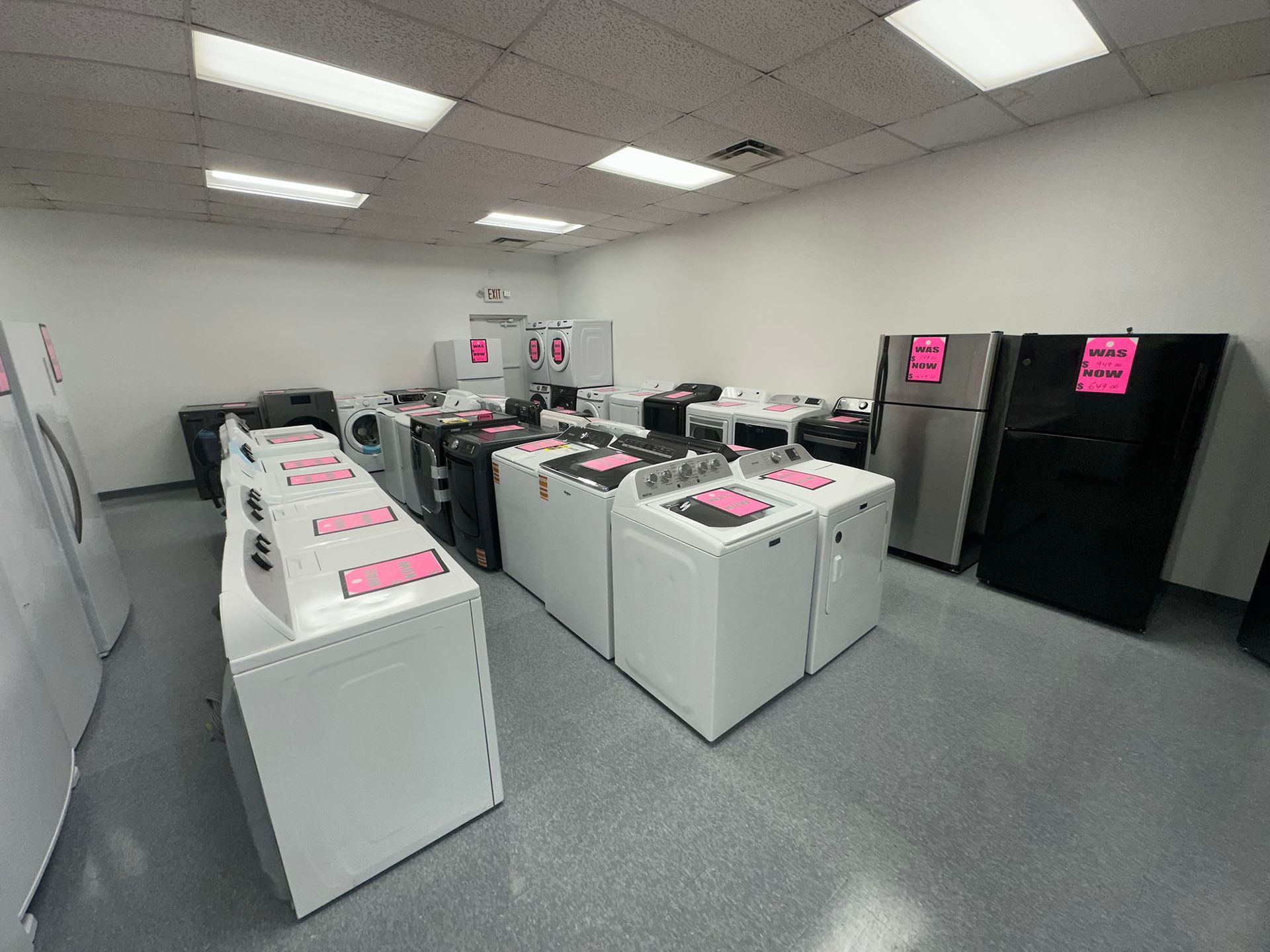 Rows of white and black washing machines in a laundromat with pink price signs under bright ceiling lights
