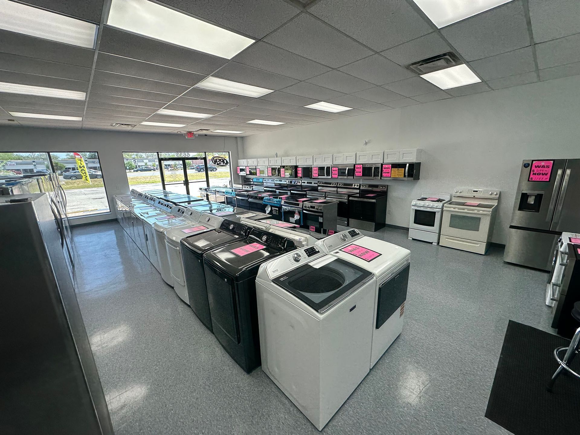 Bright laundry room with rows of washers and dryers, gray floor, and large front windows.