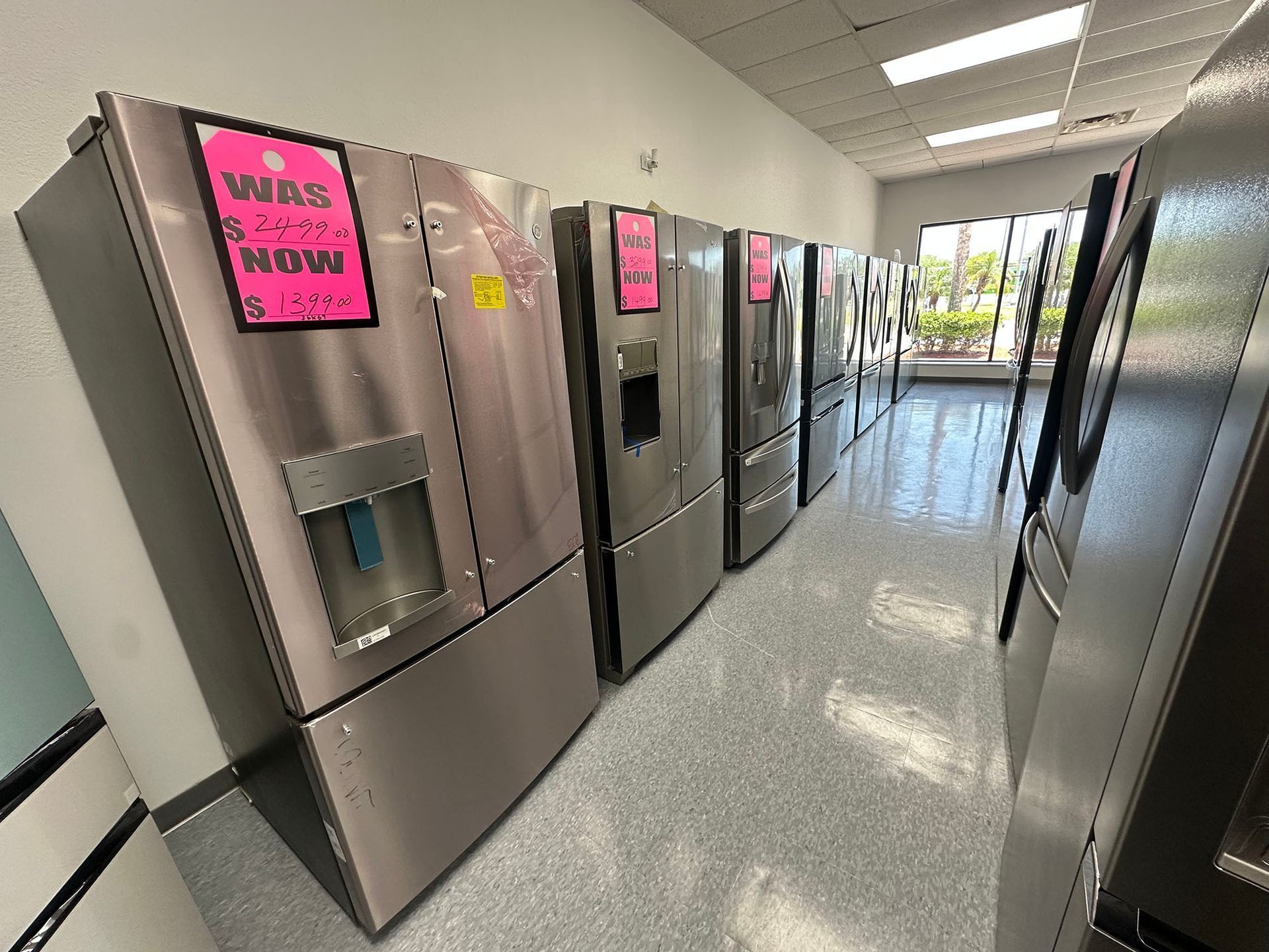 Row of stainless steel refrigerators in a bright hallway, with pink sale signs on several doors.