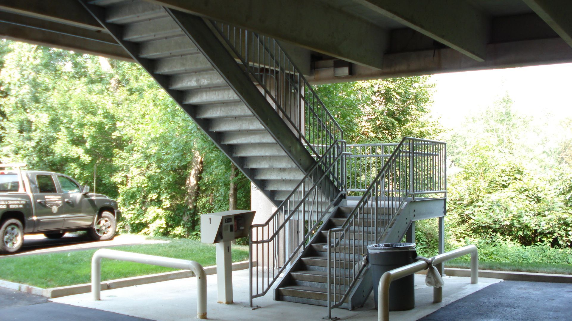 A set of stairs leading up to a parking garage under a bridge