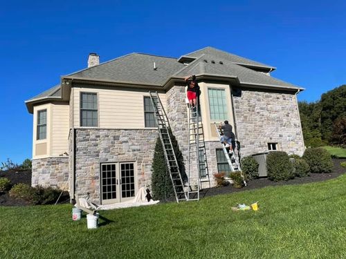 Two workers on ladders painting a stone house exterior on a sunny day