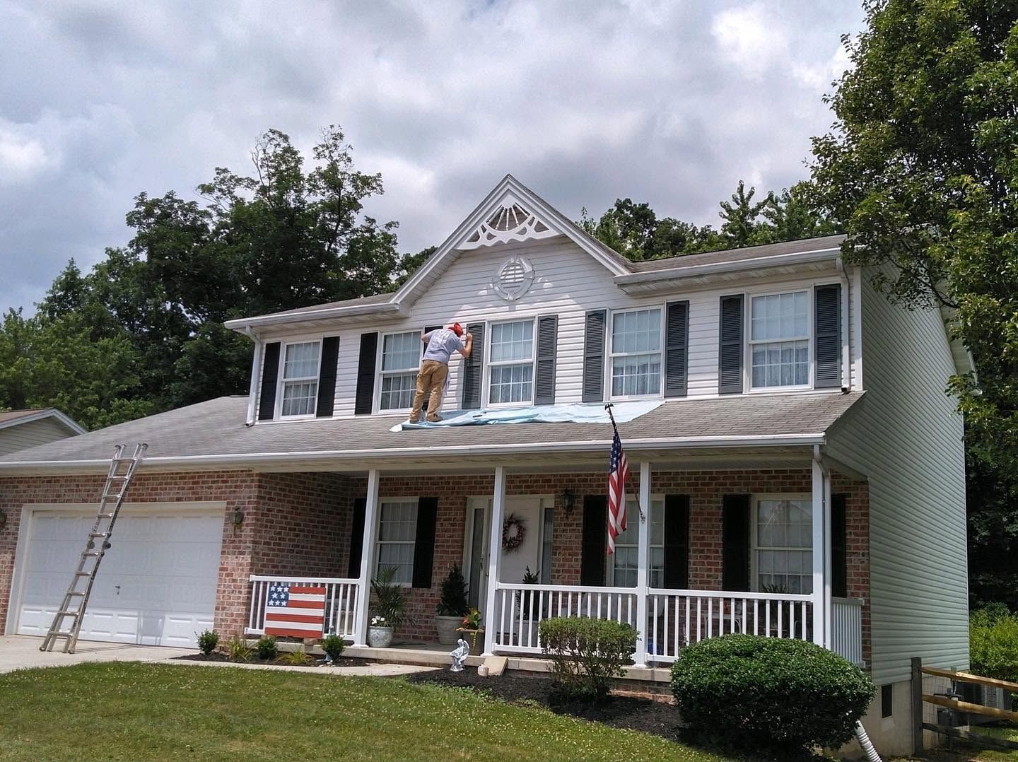 Two-story suburban house with white siding, brick garage, porch, and workers on the roof.