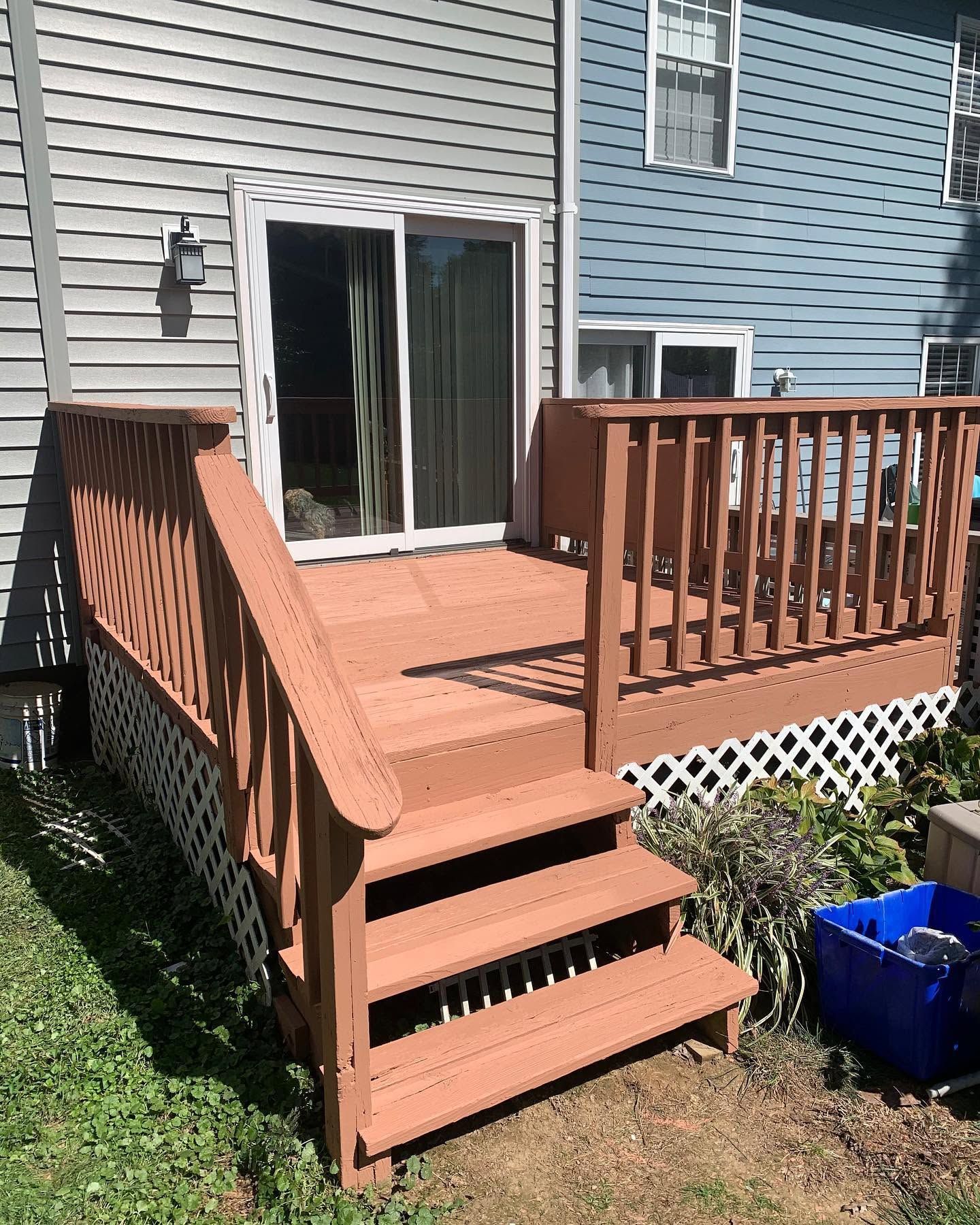 Wooden backyard deck with steps and railing leading to sliding glass doors on a house