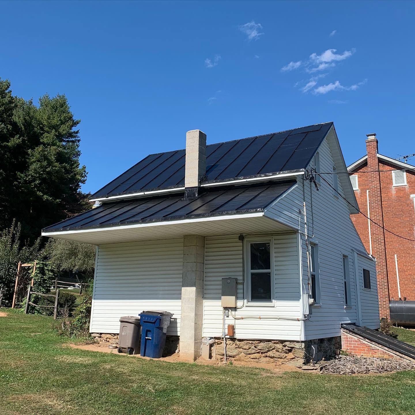 Small white house with a dark metal roof and solar panels, viewed from the front under a blue sky