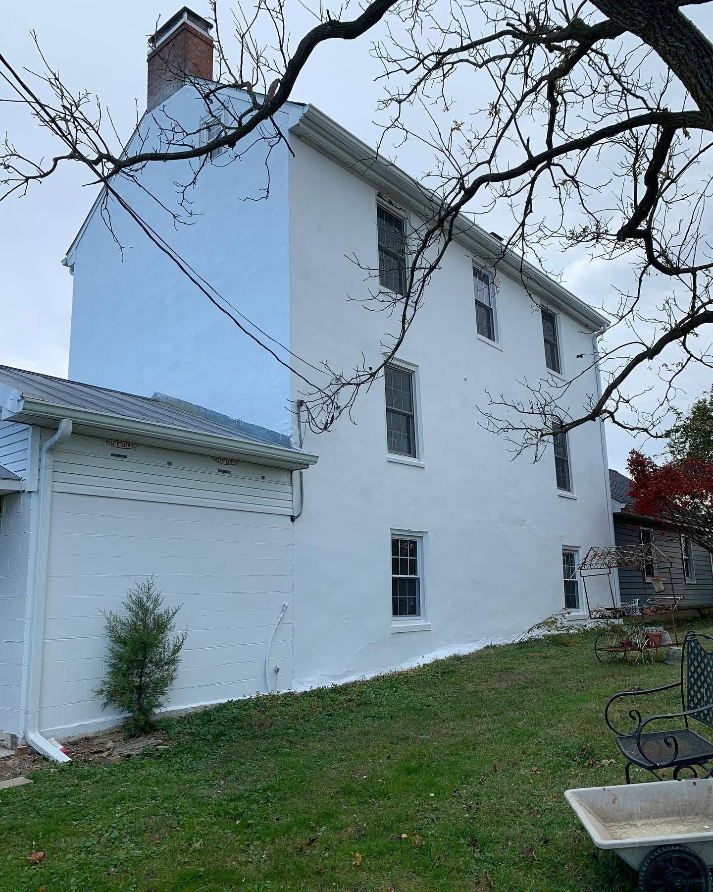 White multi-story house with a garage, viewed from a grassy yard with bare tree branches overhead.