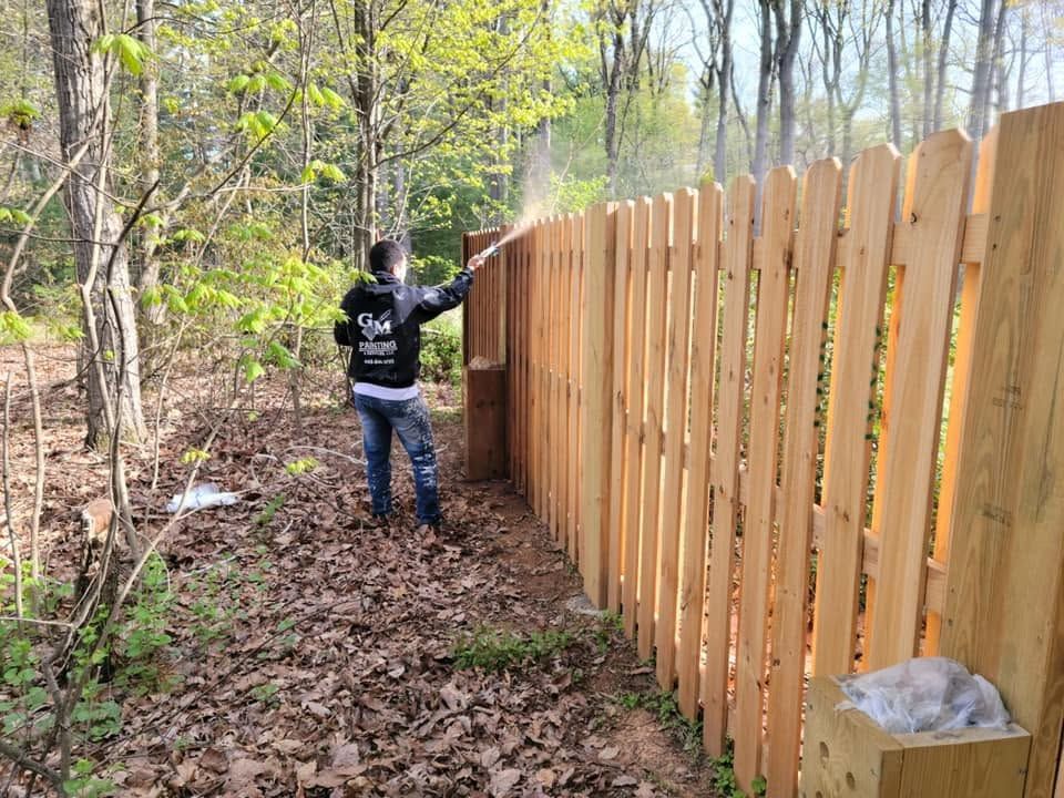 Person staining a wooden fence along a wooded yard in autumn