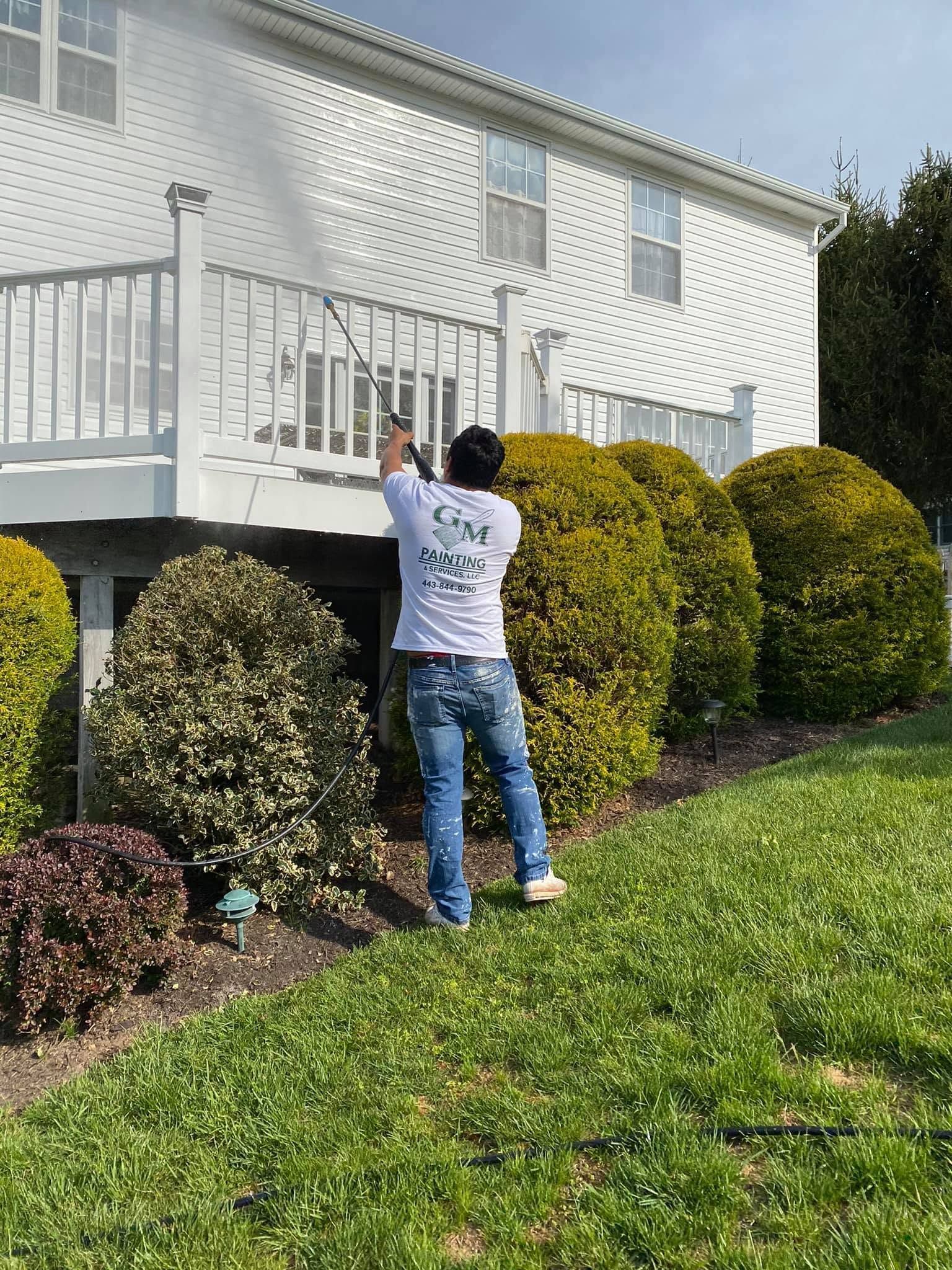 Person reaching up toward a white house deck amid green shrubs and lawn