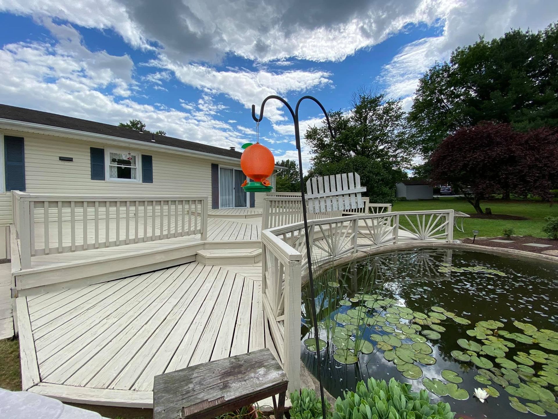 White deck beside a lily pond in a backyard, with an orange lantern and cloudy sky