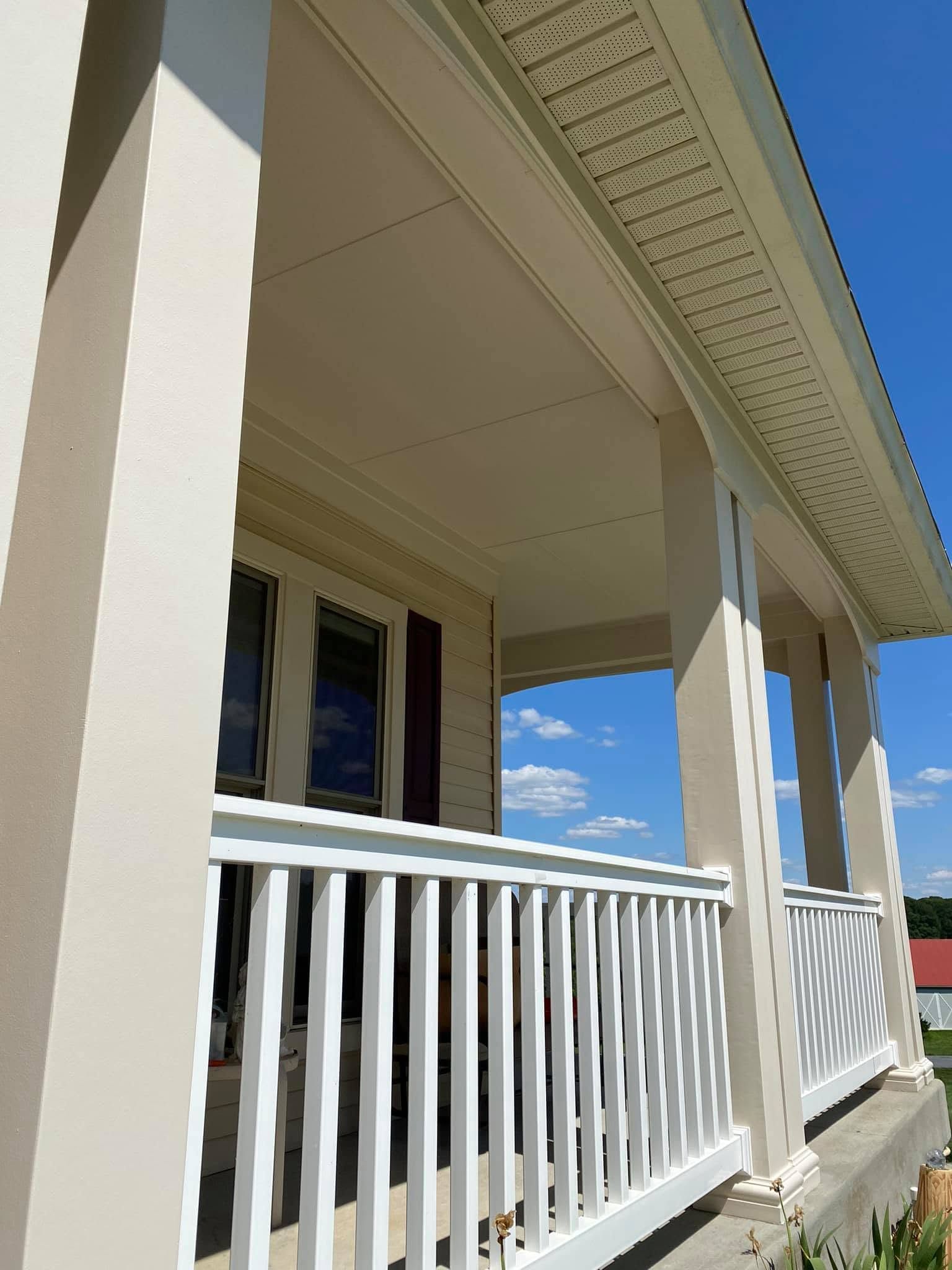 White porch with railing, beige siding, and blue sky in the background