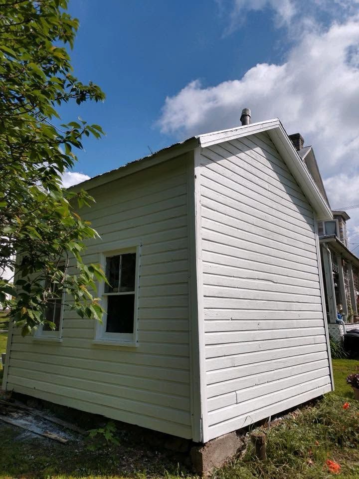 White vinyl-sided house exterior with a gabled roof, viewed from the side under a blue sky
