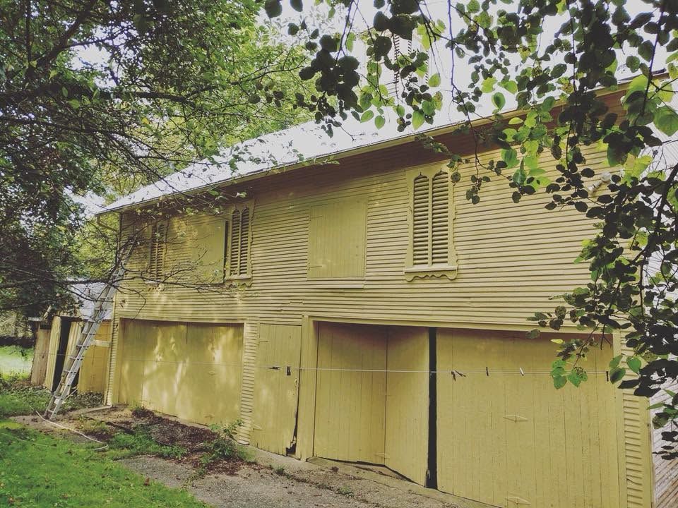 Yellow two-story house with a garage, viewed from the side under leafy trees.