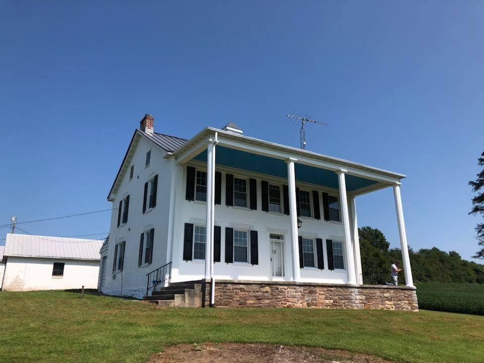 White farmhouse with a stone porch on a grassy hill under a clear blue sky