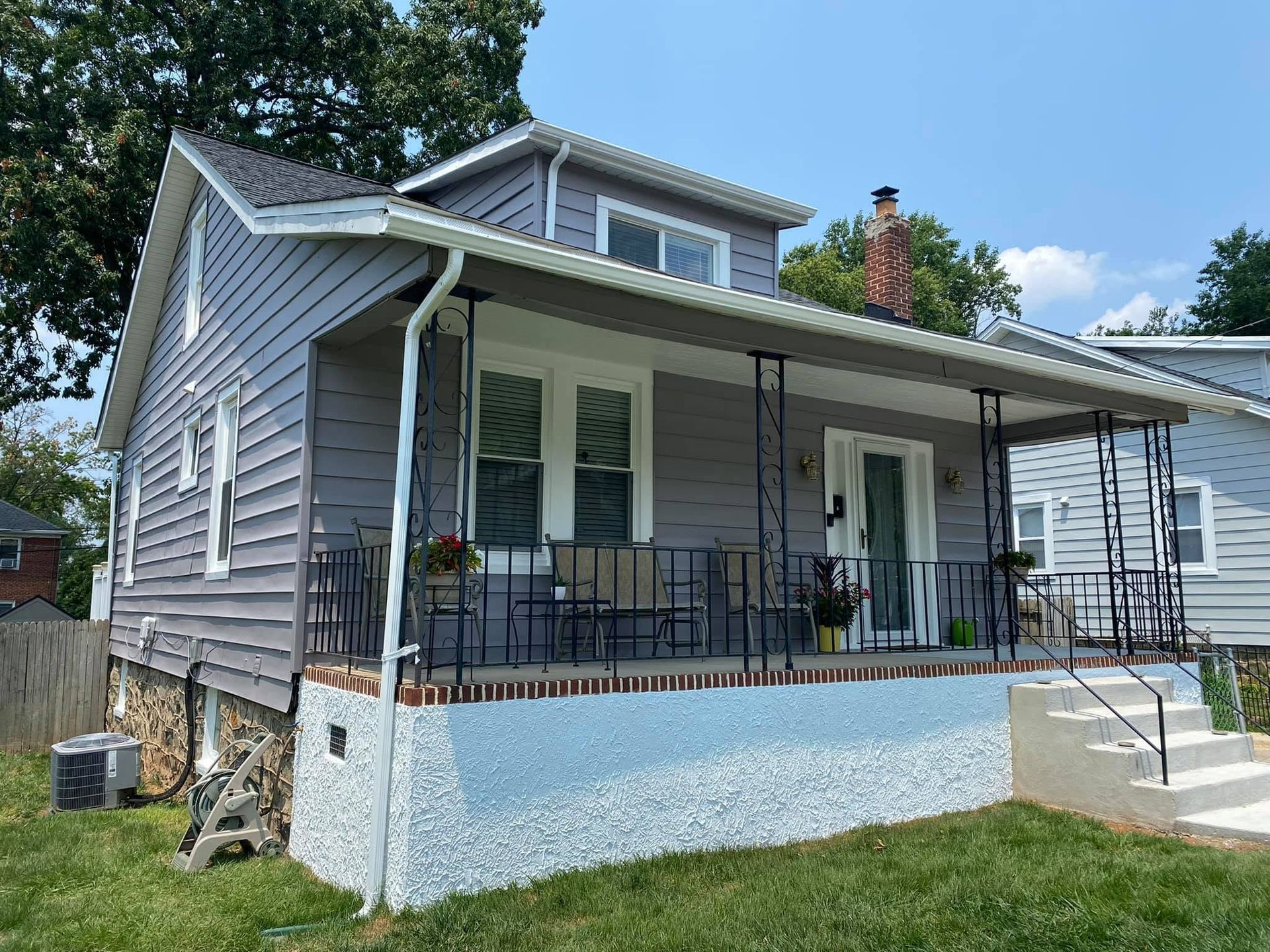 Gray house with white porch railing, front steps, and a brick chimney under a blue sky