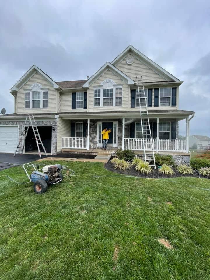 Two-story gray house with front porch; lawn mower on green yard and ladder by the garage during exterior work