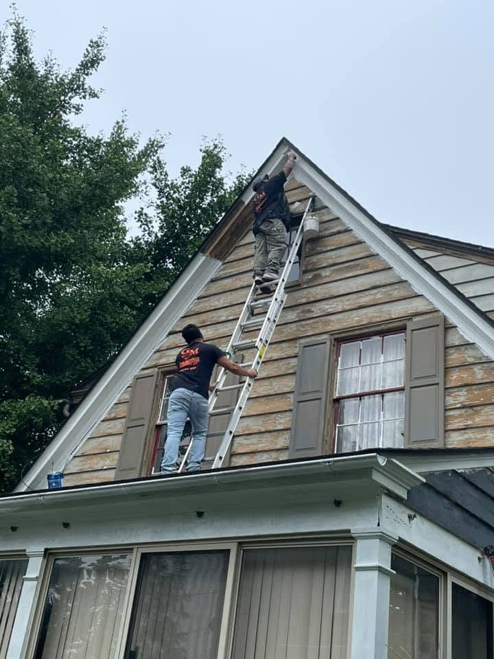 Two workers on ladders repairing the roof of a house with wood siding