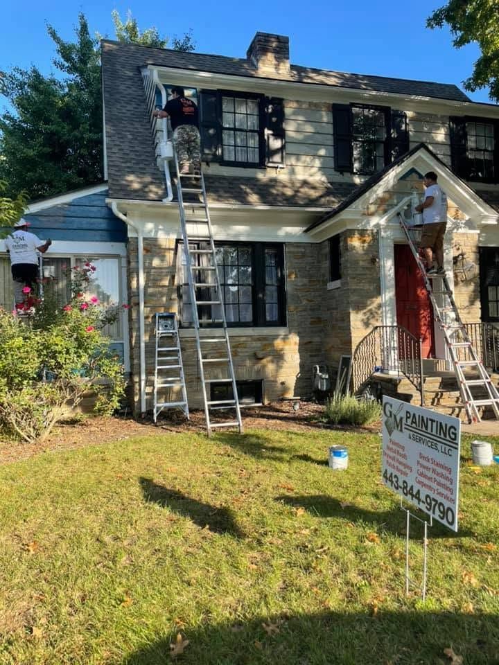 Workers on ladders painting a two-story house with a yard sign in front.