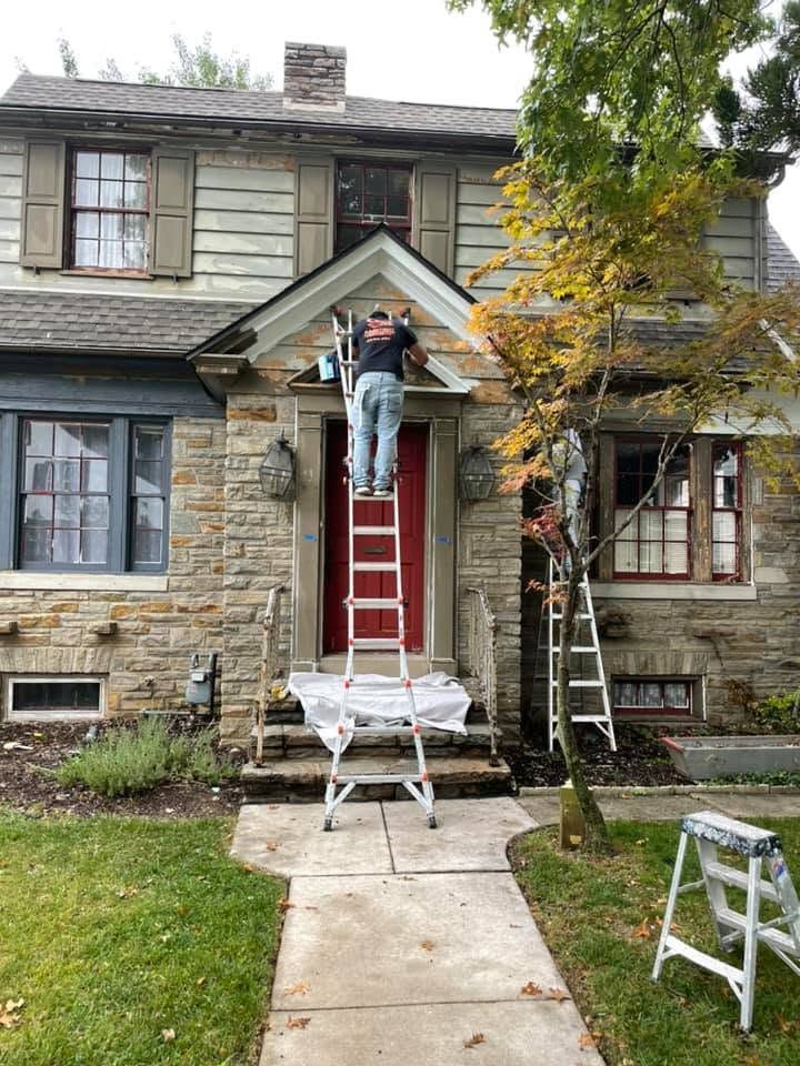 Person on ladder painting a red front door on a stone house