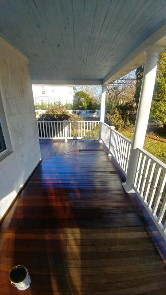 Covered wooden porch with white railings and sunlit dark-stained floorboards.