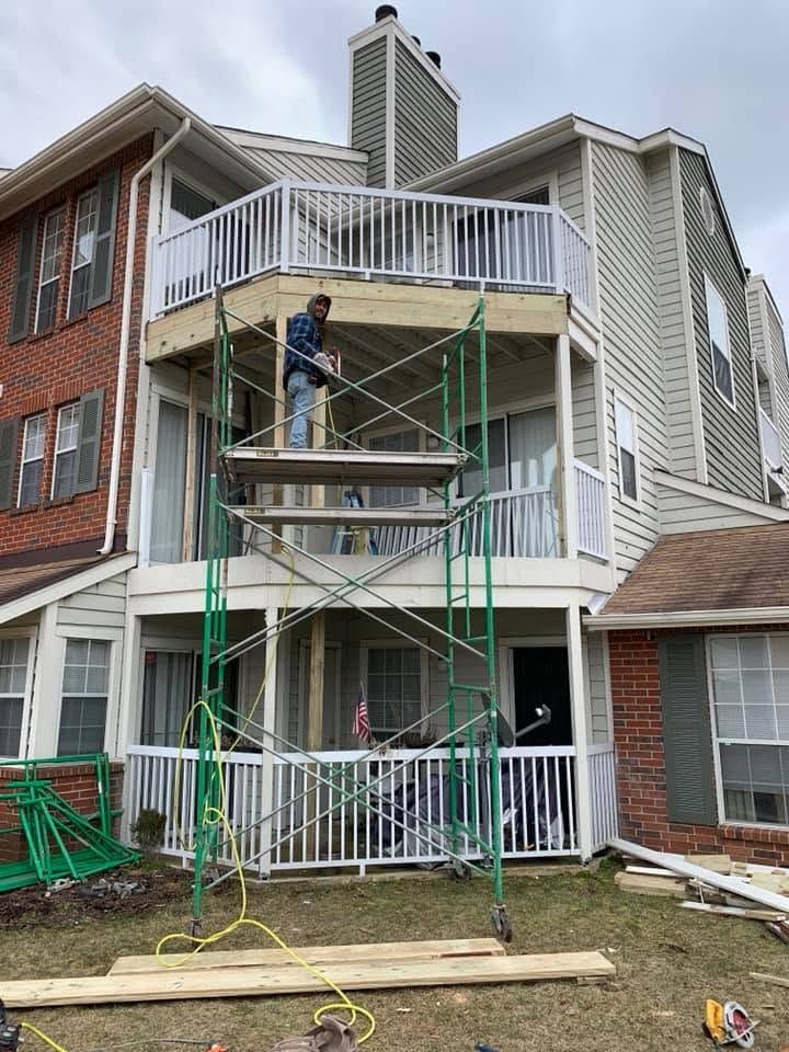 Workers on scaffolding painting an apartment building exterior with white railings and gray siding