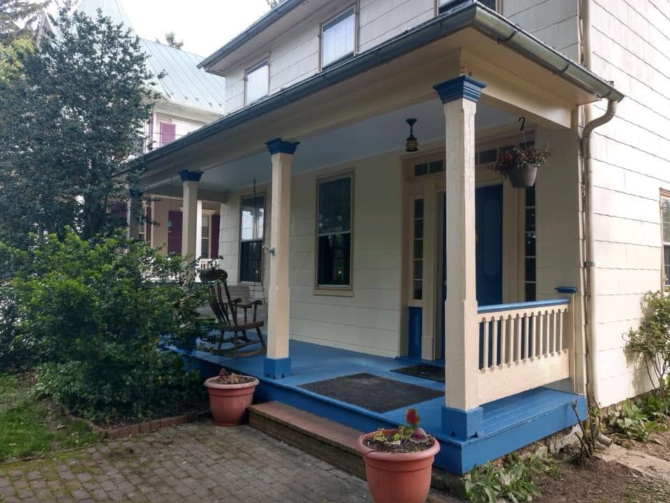 Small beige house porch with blue trim, white columns, potted plants, and a hanging lantern
