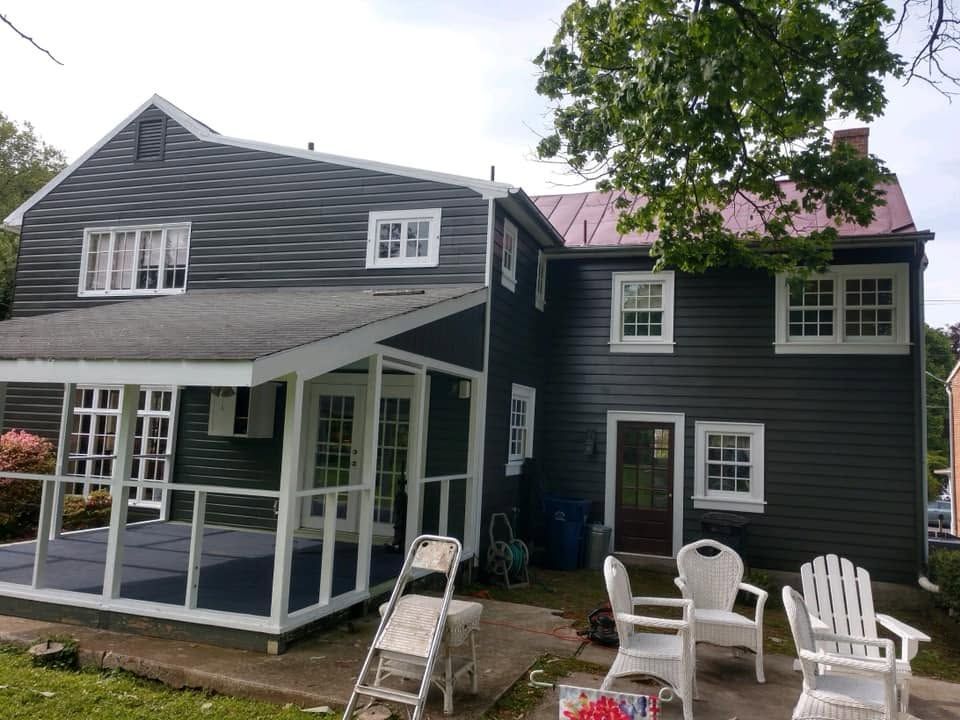 Dark gray house with white trim, porch, and patio chairs under a tree.