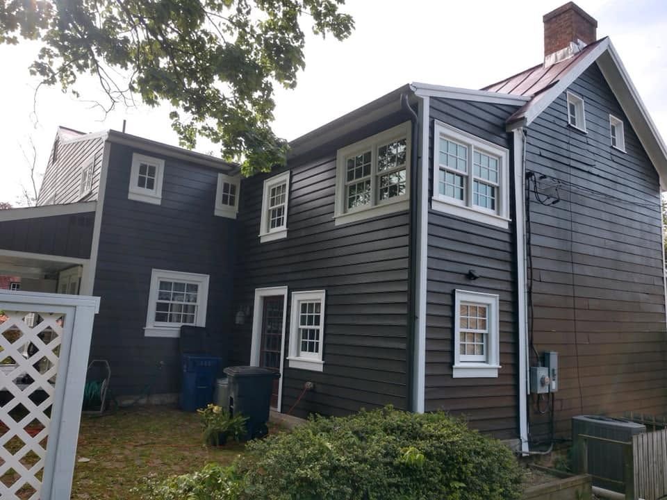 Dark blue house exterior with white-trim windows, a chimney, and a small yard under cloudy skies.