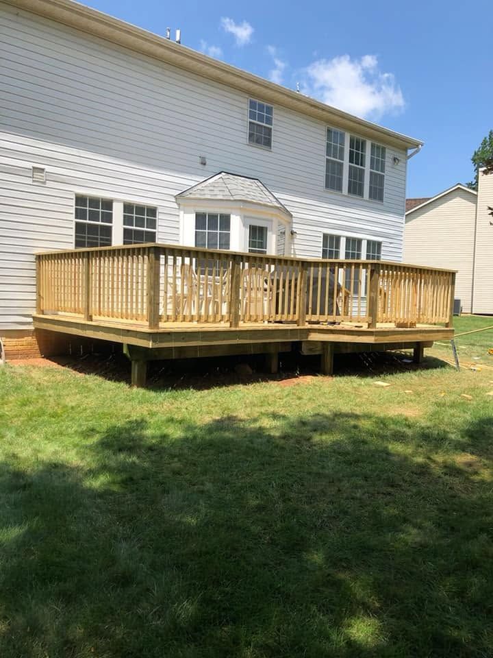 Wooden deck with railings attached to the back of a white house on a grassy yard
