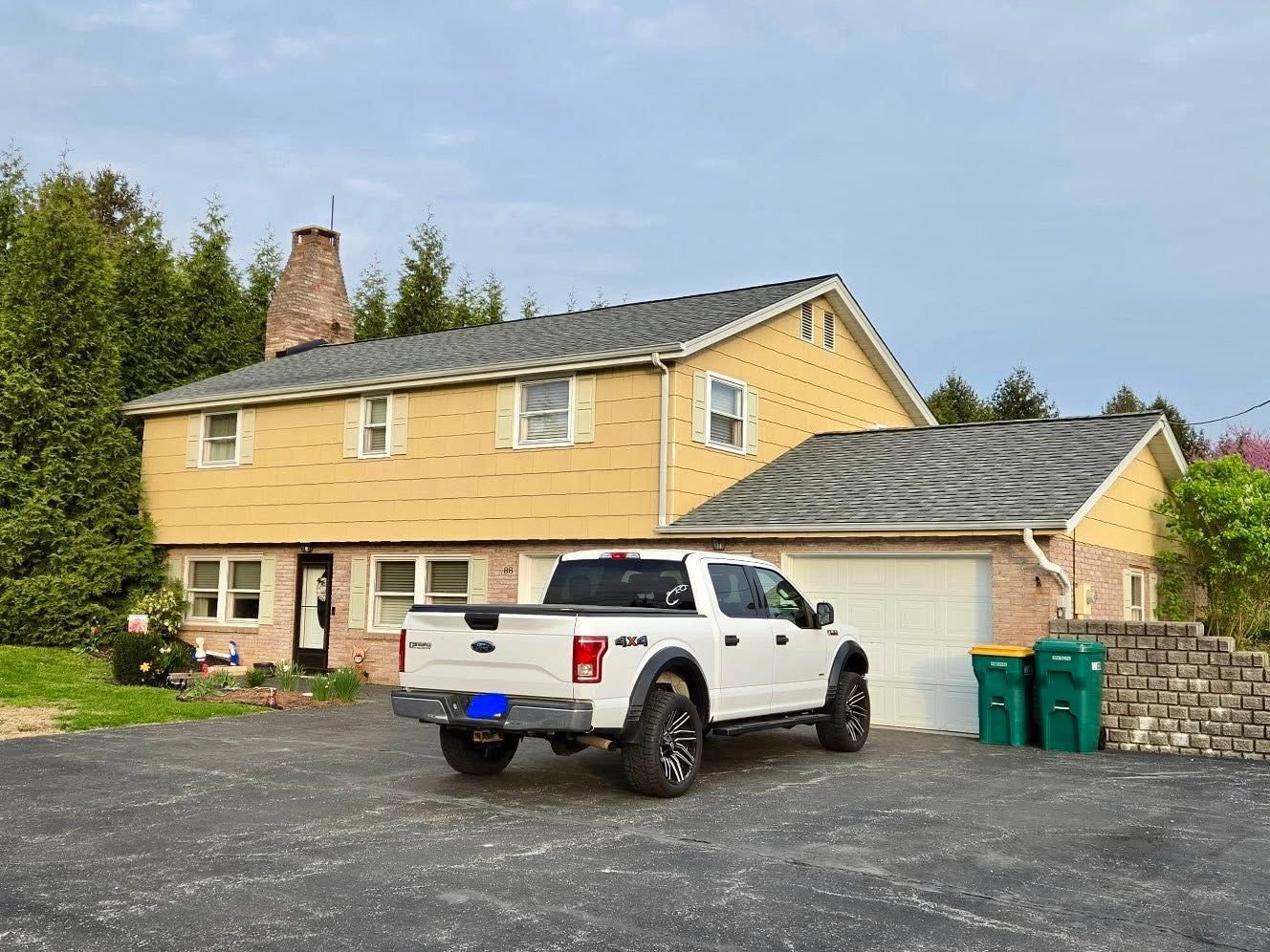 White pickup in front of a yellow two-story house with attached garage and gravel driveway